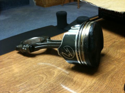 1972 Ford Ranchero - A piston and connecting rod assembly, a distinctive lightning bolt emblem, rests on a wooden table.