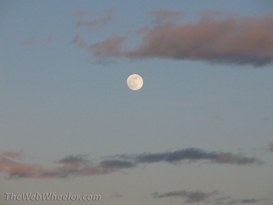 Full moon in a pale blue sky with scattered clouds