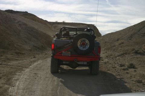 1991 Ford Bronco - A 1991 Ford Bronco navigates a dusty trail through a barren, hilly terrain under a partly cloudy sky.