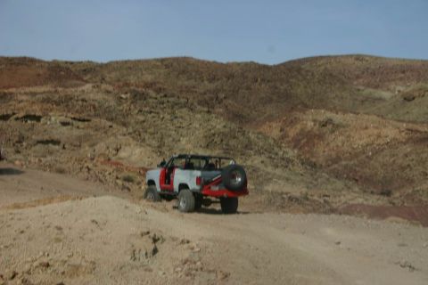 1991 Ford Bronco - An off-road vehicle with its doors removed navigates a dusty desert terrain under a clear blue sky.