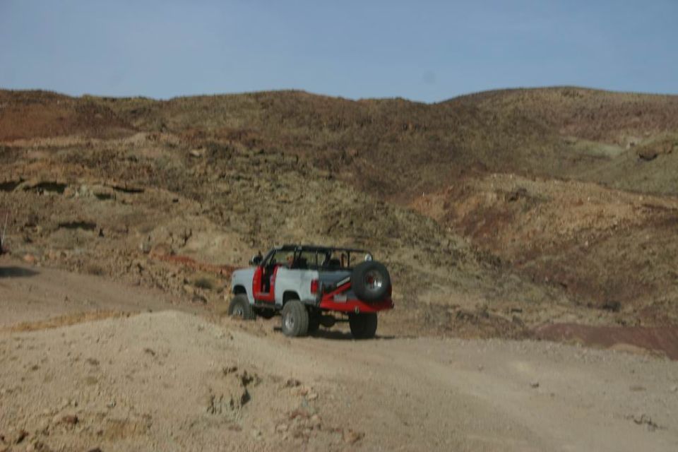 White and red off-road vehicle with spare tire on back, doors removed, driving on dirt road in desert