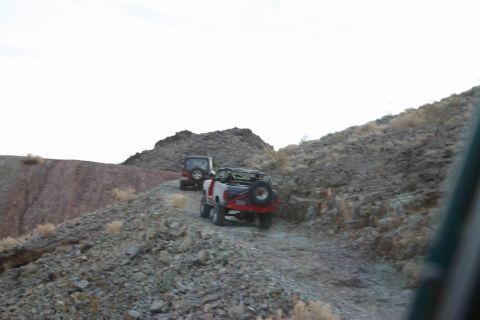 1991 Ford Bronco - Two off-road vehicles navigate a , rocky trail under a bright sky.