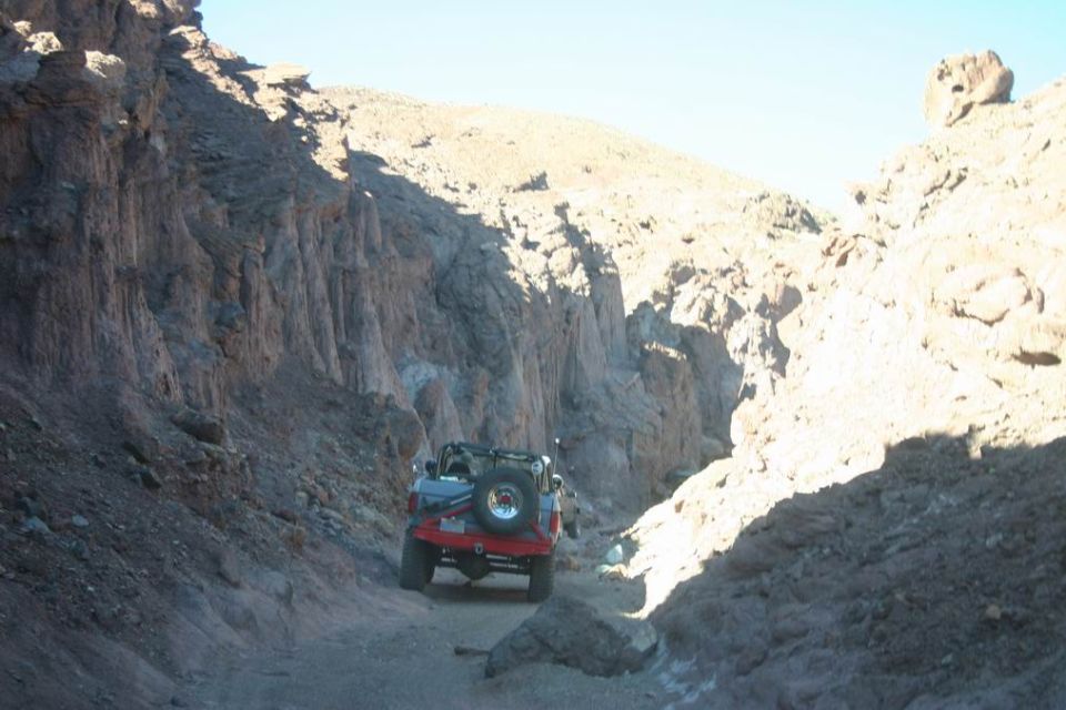 Jeep Wrangler with spare tire on back driving on dirt road in canyon