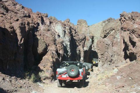 1991 Ford Bronco - Multiple off-road vehicles navigate a tight passage through a , rocky canyon under a clear blue sky.