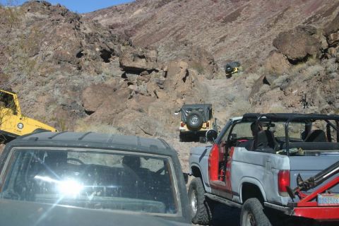 1991 Ford Bronco - Multiple off-road vehicles navigate a rocky mountain trail under a clear blue sky.