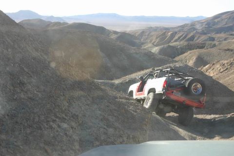 1991 Ford Bronco - A modified off-road vehicle navigates a challenging incline in a barren, mountainous desert environment.