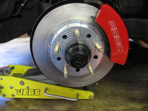 1990 Chevrolet Silverado 1500 - A close-up view of a vehicle's brake system, showing a red caliper and rotor, with a yellow jack supporting it.