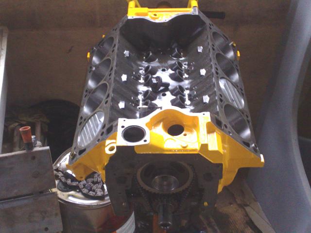 Engine block painted yellow, hanging from a hoist. Cylinders are visible