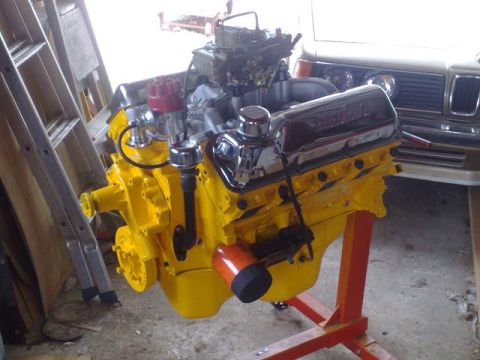 1978 Ford Bronco - A yellow V8 engine is displayed on an orange stand, with a ladder and another vehicle visible in the background.