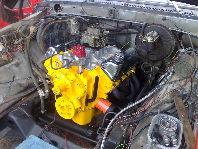 Yellow-painted V8 engine with red distributor and chrome valve cover in an engine bay under construction