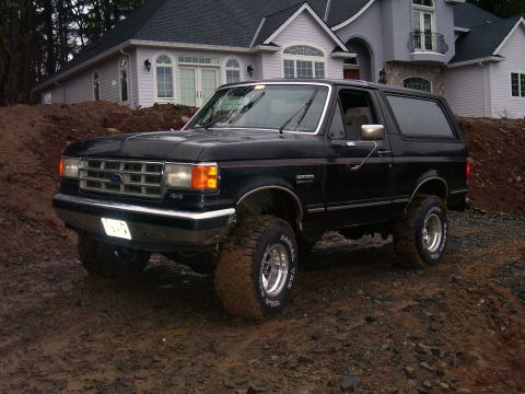 1988 Ford Bronco - This black Ford Bronco is shown in a three-quarter front view, parked on a dirt mound in front of a house.