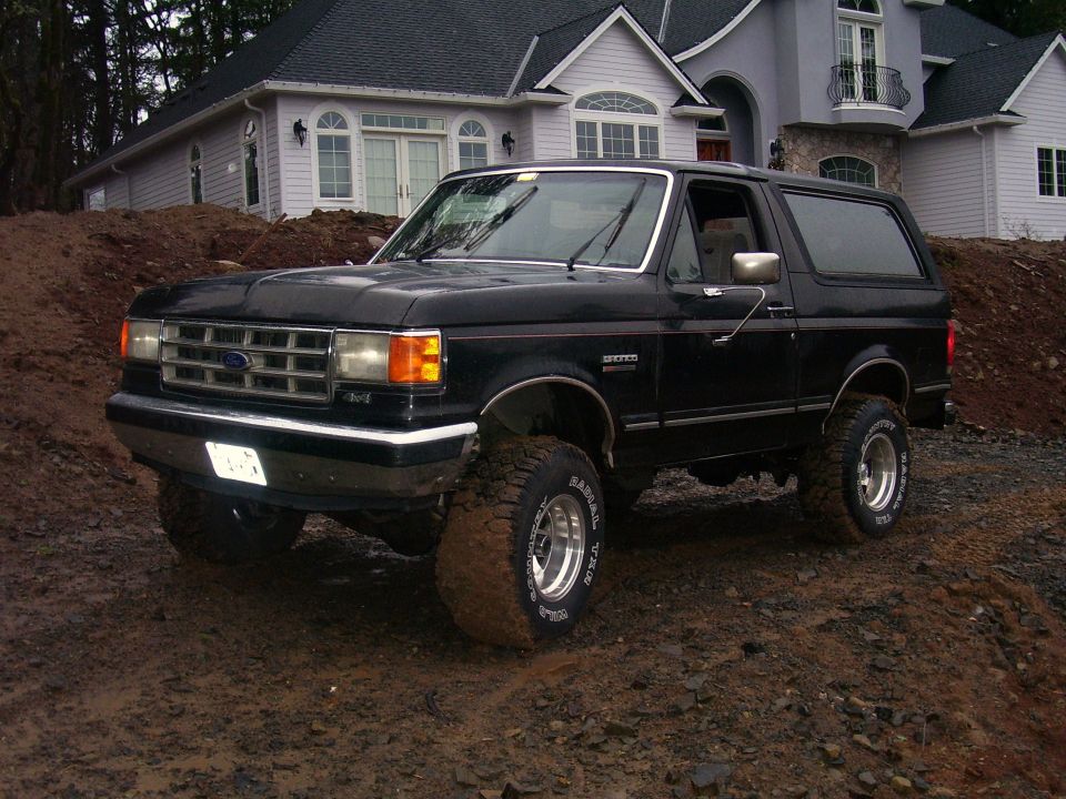 Black Ford Bronco with aftermarket wheels parked on a dirt mound