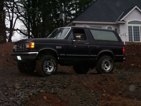1988 Ford Bronco - A black Ford Bronco is parked on a dirt hill in front of a house.