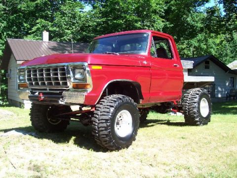 1978 Ford F-150 - This lifted pickup truck features a prominent grille and large off-road tires, set against a backdrop of trees and houses.