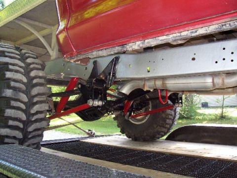 1978 Ford F-150 - The underside of a red truck shows heavy-duty suspension and large tires, suggesting off-road modifications.