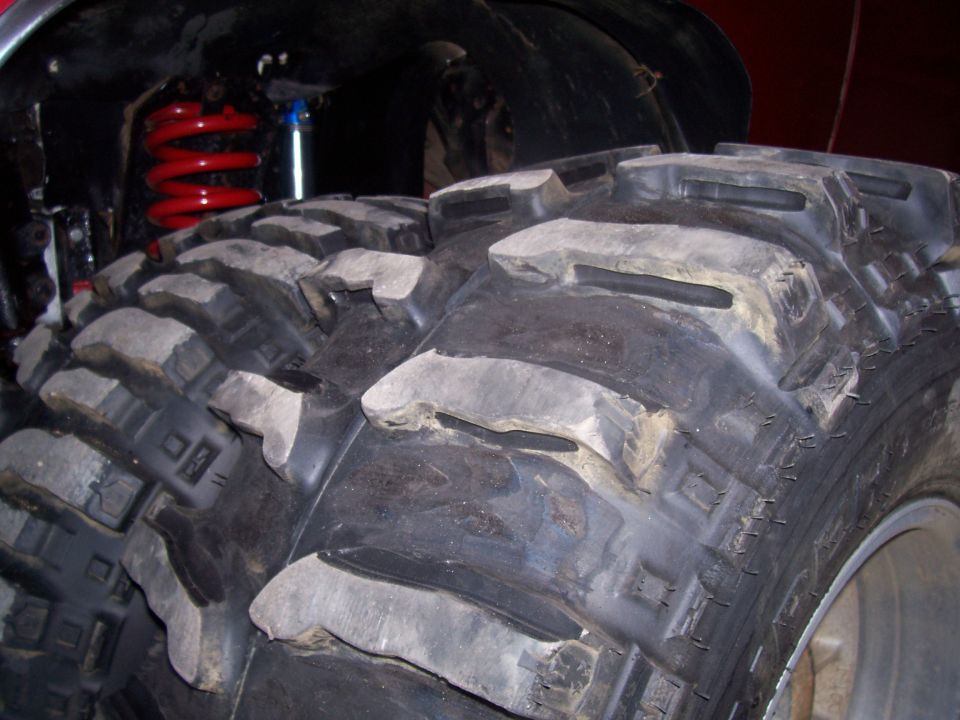 Close-up of large off-road tires with red coil springs and blue shock absorber visible