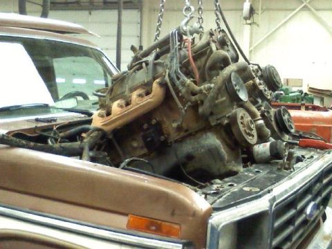 1985 Ford Bronco - An engine is hoisted out of a brown SUV in a workshop.