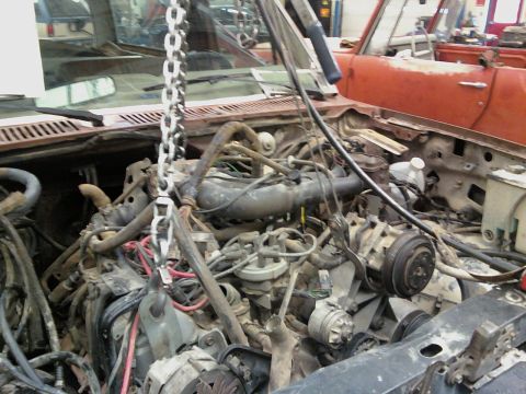 1985 Ford Bronco - Engine bay of a vehicle being worked on, with an engine hoist overhead and visible wiring and components.