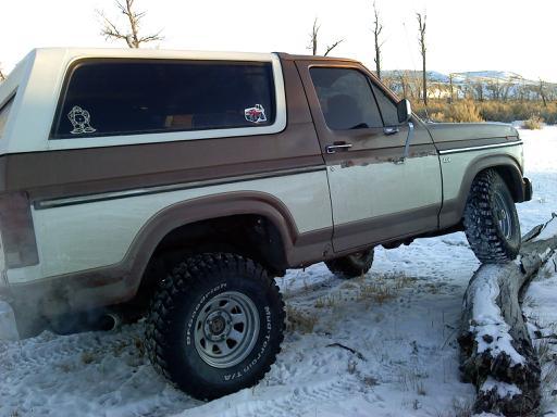 1985 Ford Bronco driving over a log in the snow