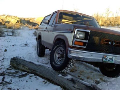 1985 Ford Bronco - This vintage Ford Bronco is navigating a snowy, off-road path with a large log obstructing the way.
