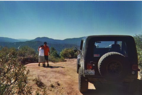 1986 Ford Bronco - A black Jeep CJ-7 is parked on a dirt road overlooking a scenic mountain landscape.
