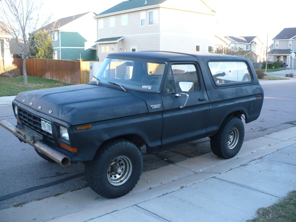 Flat-black Ford Bronco 4x4 with hardtop, 3/4 front view parked curbside in a suburb
