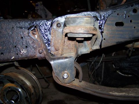 1989 Ford F-150 - This image shows a close-up view of a heavily rusted truck frame, focusing on suspension components and a detached wheel rim.