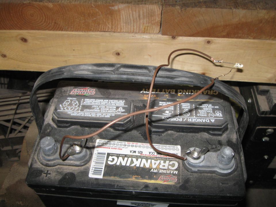 Car battery with wires connected to terminals and a small LED light