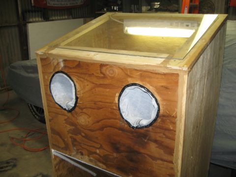 2004 Aston Martin Virage - A wooden sandblaster cabinet with two glove ports and a fluorescent light overhead is visible, with a tarp-covered object in the background.