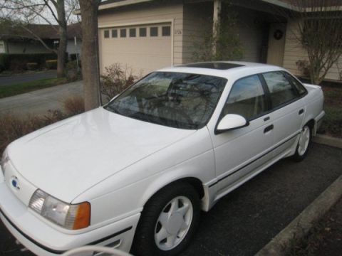 1993 Ford Taurus - A white sedan is parked in front of a garage, viewed from the front-left.