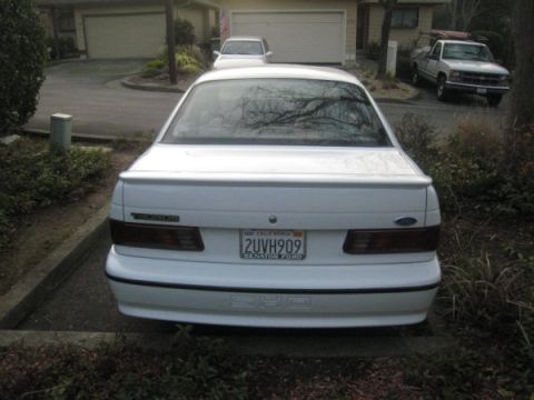 1993 Ford Taurus - The rear of a white 1993 Ford Taurus is shown, with a license plate and taillights visible.