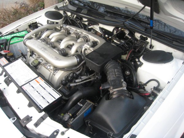 Engine bay of a white car, showing the V6 engine, air intake, and battery