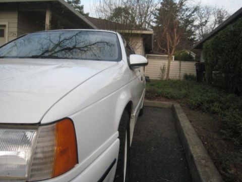 1993 Ford Taurus - A white sedan is parked in a residential driveway, showing its front quarter panel and headlight.