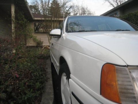 1993 Ford Taurus - A white 1993 Ford Taurus is parked in a driveway next to a house.