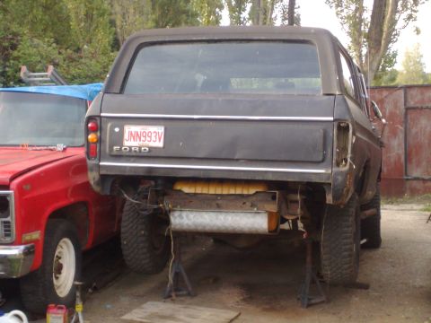 1978 Ford Bronco - Rear view of a dark 1978 Ford Bronco undergoing repairs, parked next to a red truck.