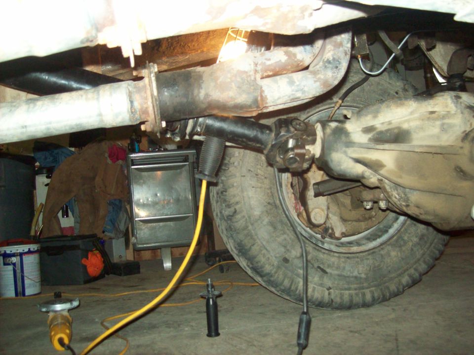 Underside of a vehicle showing a drive shaft connected to a rear axle, with a tire visible