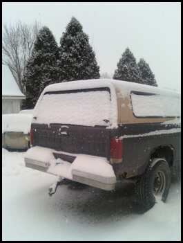 1996 Ford Bronco - A dark colored SUV with a camper shell is seen from the rear, covered in snow.