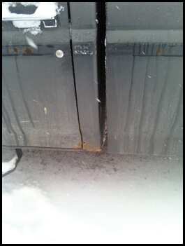 1996 Ford Bronco - Close-up of a car door seam showing rust and dirt, with snow on the ground.