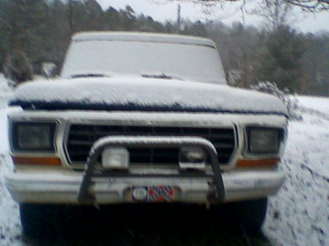 White Ford truck covered in snow, front view, with a brush guard and auxiliary lights