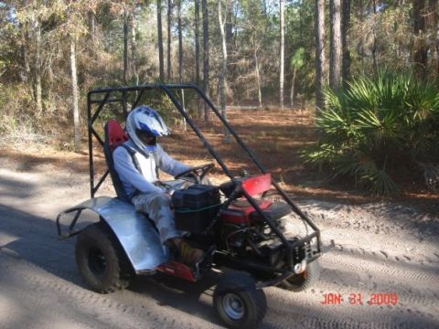 2001 Ford F-150 - Go-kart with roll cage and driver wearing helmet on dirt path in wooded area.