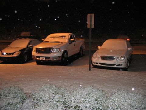 2004 Ford F-150 - Three vehicles covered in snow are parked outside at night, with snowflakes falling.