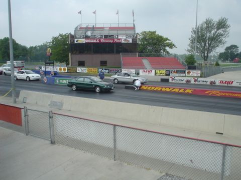 1999 Ford Taurus - Two sedans race on a track at Norwalk Raceway Park, with spectators in the grandstands.