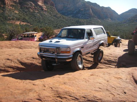 1996 Ford Bronco - A white 1996 Ford Bronco navigates a rocky trail, with other off-road vehicles visible in the background.