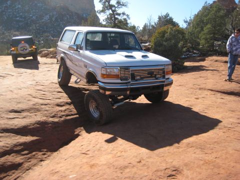 1996 Ford Bronco - White Ford Bronco with lifted suspension on rocky terrain, another SUV in background.