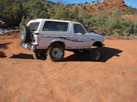 1996 Ford Bronco - A white 1996 Ford Bronco is parked on a dirt road with a spare tire mounted on the rear.