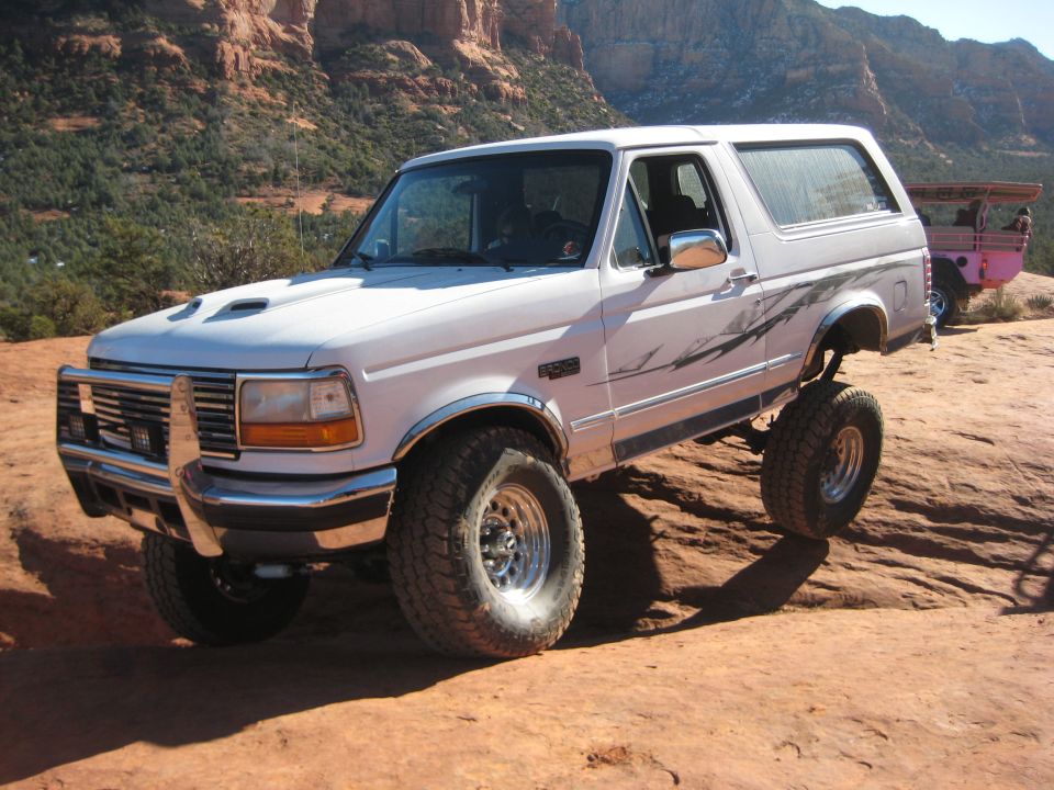 White 1996 Ford Bronco with lifted suspension and off-road tires on rocky terrain