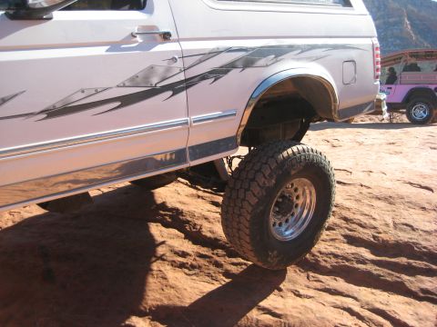 1996 Ford Bronco - A lifted white SUV with tribal graphics is parked on a rocky surface, with a pink Jeep in the background.