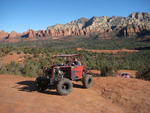 1996 Ford Bronco - A custom red off-road buggy with flame decals and an exposed engine is seen on a dirt trail, with another pink vehicle in the distance and…