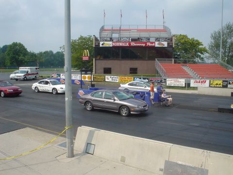 1999 Ford Taurus - A gray sedan is on the race track at Norwalk Raceway Park, with spectators in the background.
