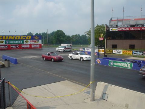 1999 Ford Taurus - A white sedan with racing stripes drives on a track at Norwalk Raceway Park.